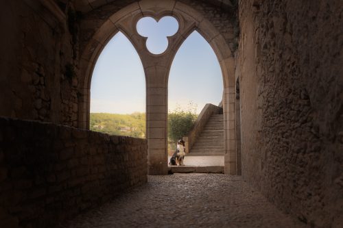 Berger australien assis sous les arches de Rocamadour